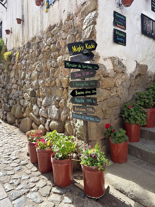 Street in Cusco with plants and a sign with arrows pointing towards different sites