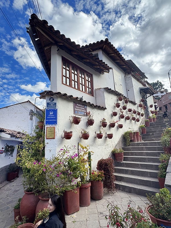 Siete Borreguitos street in Cusco Peru - red pots with plants hanging on a white building with stairs running alongside it