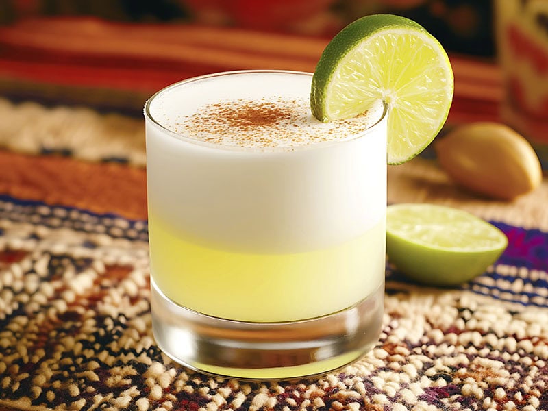 Pisco Sour cocktail with cinnamon and a lime wedge on a colorful cloth placemat